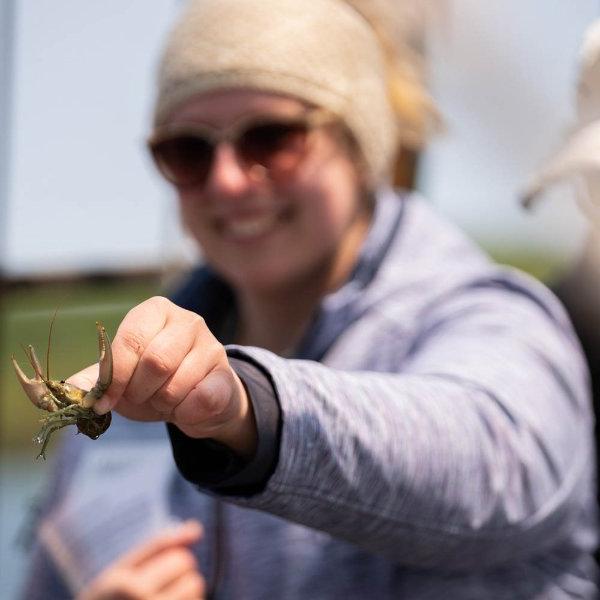 A student in sunglasses holds a crayfish while on a schooner, some species of crayfish are invasive to the waters in northern Michigan.